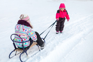 Little baby girl in pink pulling a sled with her sister