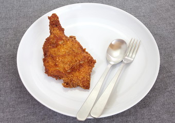 Delicious fried chicken on white plate with fork and spoon
