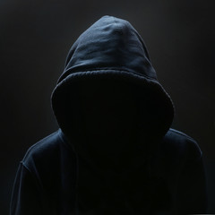 Unrecognizable person wearing hood against black background - obrazy, fototapety, plakaty