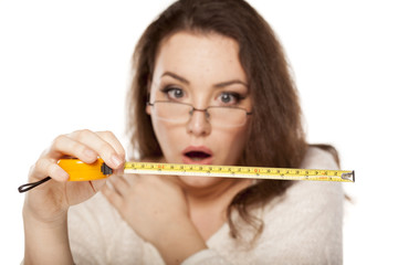 young woman is shocked by the size shown on the measuring tape