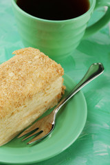 Napoleon cake on plate and cup of tea on table close-up