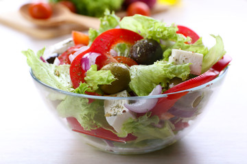 Greek salad in glass dish on wooden table background