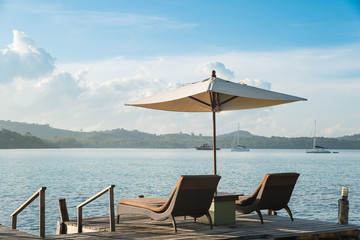 Two chairs and umbrella on wooden desk against blue sky