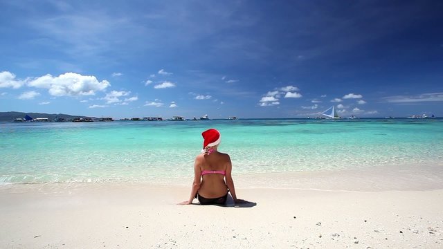 Woman in Santa Claus hat sitting on tropical beach