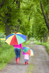 mother and her daughter with umbrellas in spring alley