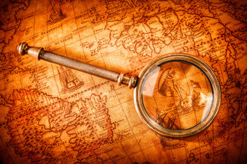 Vintage magnifying glass lies on an ancient world map