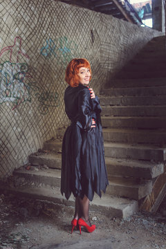 Ginger woman in black mantle in abandoned building