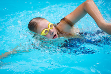 Young girl in goggles and cap swimming crawl stroke style
