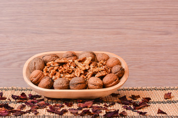 Walnuts on wooden bowl with dried rose petals on table