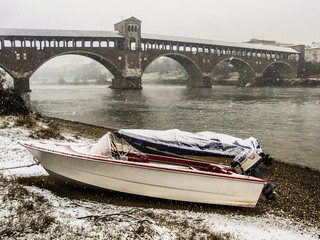 Two boats along the shores of river Ticino in Pavia during a snowfall