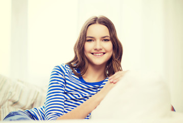 Naklejka premium smiling teenage girl sitting on sofa at home