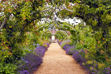 Colourful English summer flower garden with a path under archway - 75610069