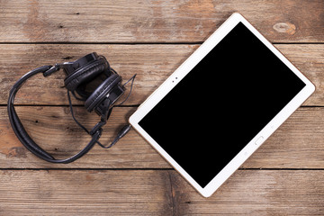 Tablet computer with headphones against wooden background