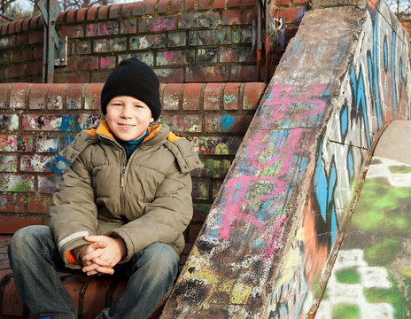 Junge sitzt vor Graffitimauer