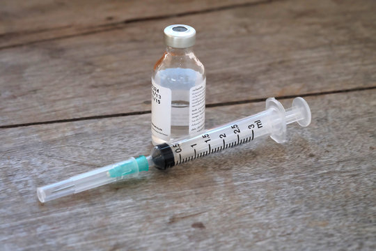 Vaccine in vial with syringe on wooden background