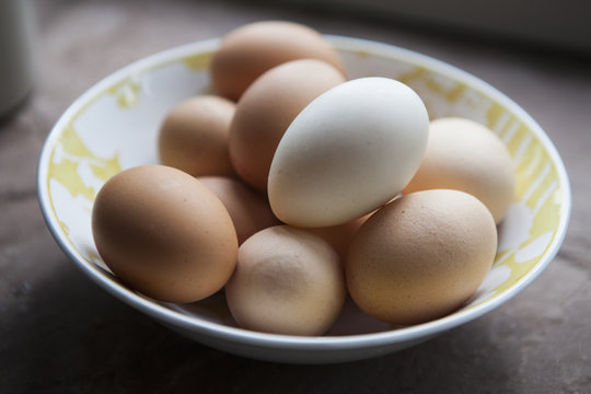 A bowl of eggs with pale and brown shells. 