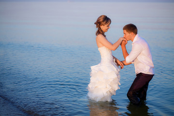bride in wedding dress and groom pose standing in sea water 