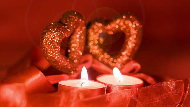 Valentines day,  two candles burning in front of hearts, closeup