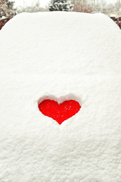 Valentine love red heart shape in snow on red car hood.
