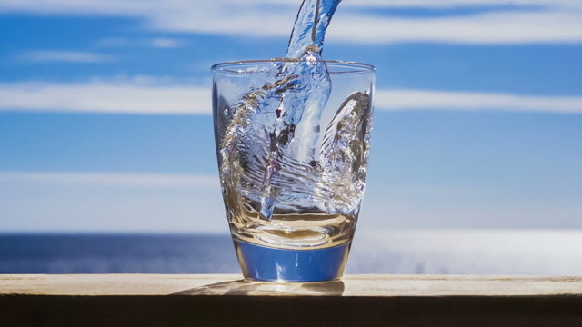 Blue water is flowing into the glass forming splashes