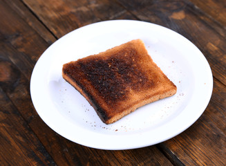 Burnt toast bread on plate, on wooden table background