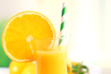 Glass of orange juice with straw and slices on bright