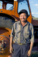 Fototapeta na wymiar Smiling Mongolian Farmer Standing Next To The Tractor
