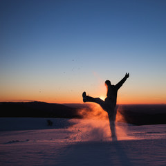 silhouetted man kicking snow in winter landscape