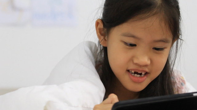 Little Asian girls using tablet on the bed, pan camera