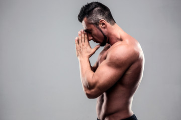 Portrait of a young muscular man praying over gray background