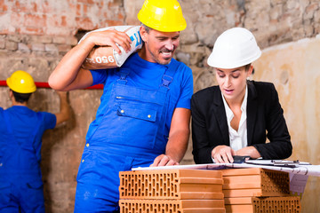 Architektin und Bauarbeiter auf Baustelle mit Bauplan
