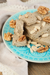 Sunflower halva with nuts on plate, on wooden background