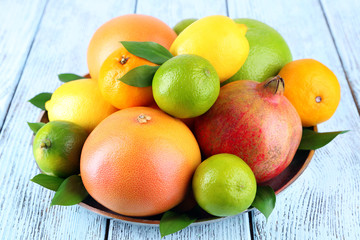 Ripe citrus with green leaves on plate on wooden background