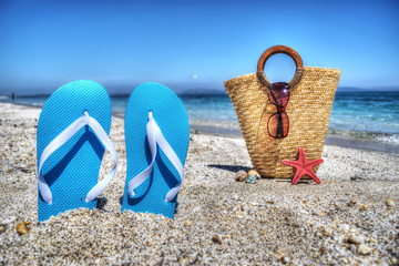 blue sandals and straw bag by the shore