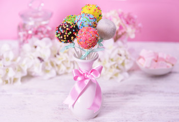 Sweet cake pops in vase on table on pink background