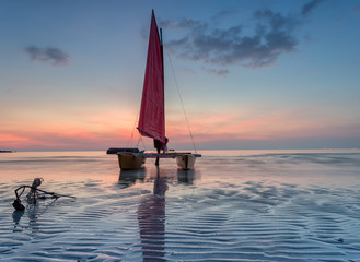 Naklejka premium Red sailboat on the beach with a beautiful sunset