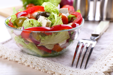 Greek salad in glass dish with fork and vegetables background