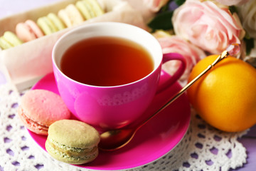 Colorful macaroons with cup of tea on wooden background
