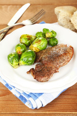 Roasted meat and vegetables on plate, on wooden table