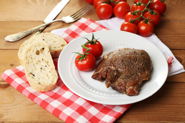 Roasted meat and vegetables on plate, on wooden table