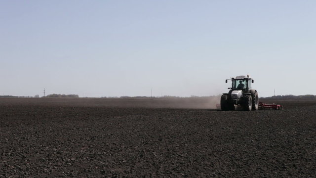 tractor plowing black field boundless with dust	