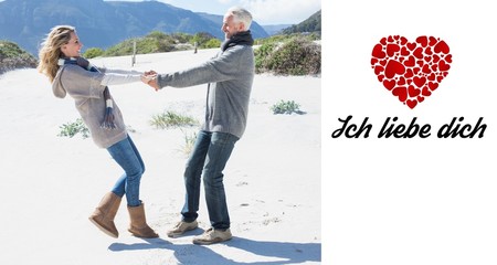 Smiling couple spinning on the beach in warm clothing