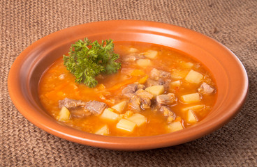 Ceramic plate of vegetable soup standing on sackcloth.