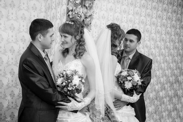 groom and the bride stand near a mirror and are reflected in it