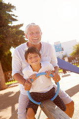 Grandfather And Grandson On Seesaw In Playground