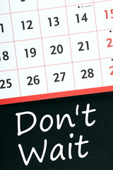 Don't Wait written on a blackboard under a wall calendar