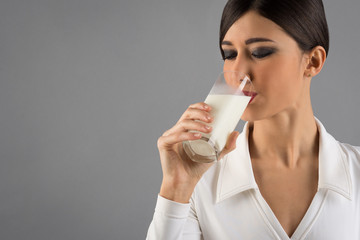 Young woman drinking milk from a glass isolated on grey backgrou