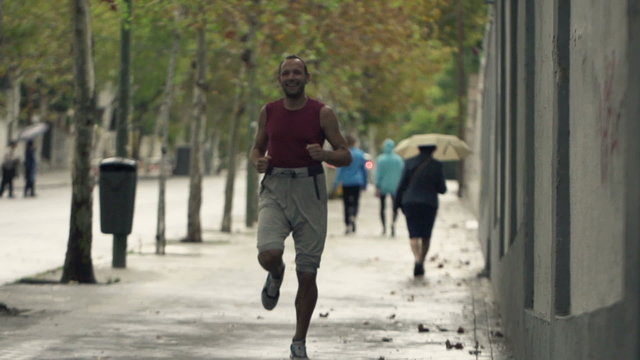 Funny, happy man jogging in city during rain