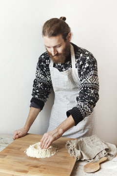 bearded stylish man with apron making dough with white flour