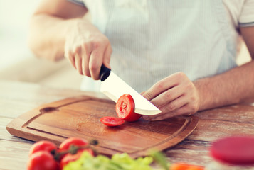 male hand cutting tomato on board with knife